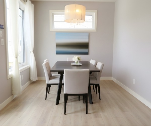 Modern dining room with light laminate flooring, white chairs and natural light from large windows.